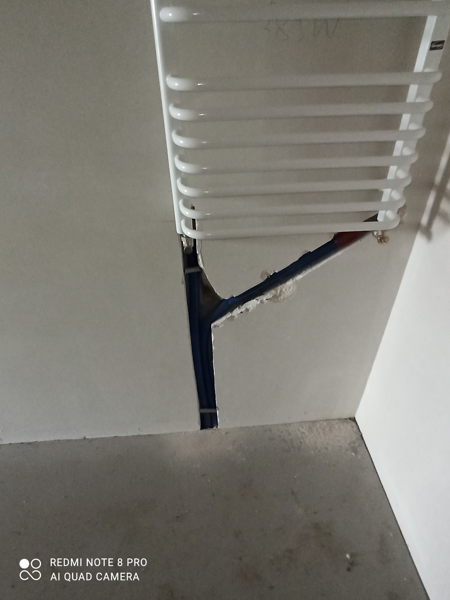 Instalacja grzejnika drabinkowego w łazience, widoczne nieotynkowane ściany i rury doprowadzające wodę.