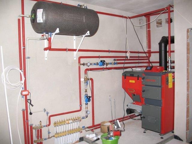 Instalacja centralnego ogrzewania z kotłem na paliwo stałe, bojlerem i rozbudowaną siecią rur w kolorze czerwonym.