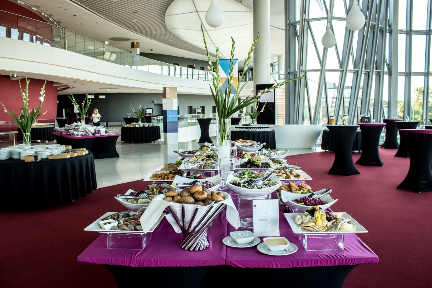 Bogato zastawiony stół z różnorodnymi potrawami cateringowymi w nowoczesnej sali konferencyjnej w Krakowie, z dekoracjami kwiatowymi i wysokimi stolikami w tle.