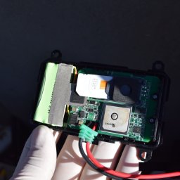DETEKTYWI Agencja Detektywistyczna Gambit - Otwarta obudowa lokalizatora GPS z kartą SIM Orange, baterią i płytką drukowaną, trzymana w dłoni w białej rękawiczce. Widoczne przewody zasilające.