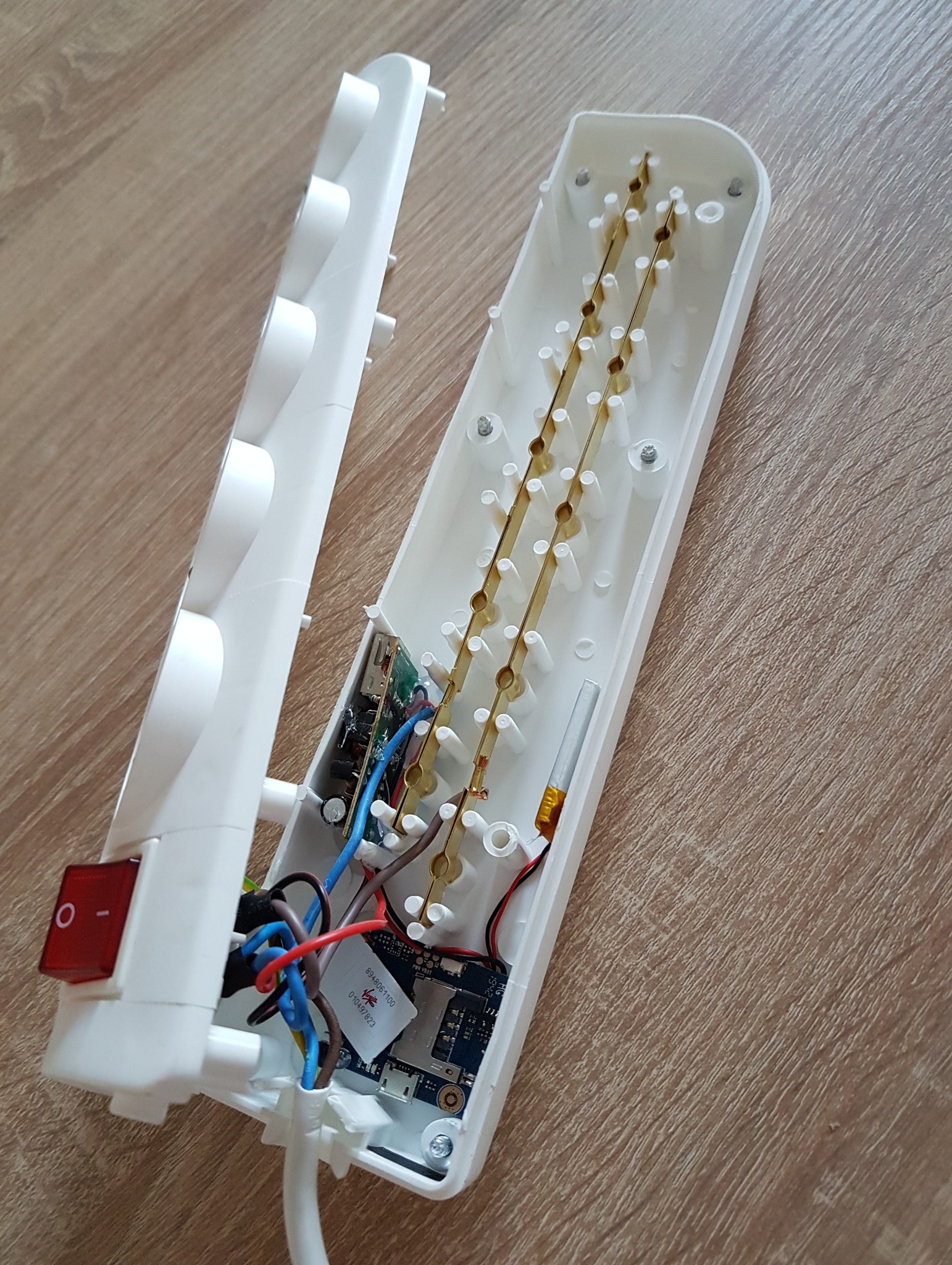 Otwarta listwa zasilająca z widocznymi elementami elektronicznymi i przewodami na drewnianym tle. Widoczny włącznik i wewnętrzna konstrukcja.