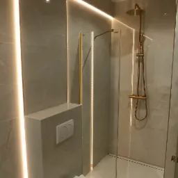 Nowoczesna łazienka w Miechucinie z podświetlanymi panelami ściennymi, kabiną prysznicową ze złotymi elementami i podwieszaną toaletą.