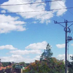 Słup elektryczny z transformatorem na tle błękitnego nieba z obłokami, widoczny znak drogowy z nazwą miejscowości Mastów II.