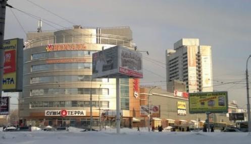 Wielopiętrowy budynek handlowy z przeszkloną fasadą i reklamami zewnętrznymi w zimowej scenerii miejskiej.