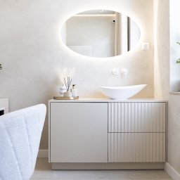 Tofi design - Nowoczesna łazienka w jasnych, stonowanych barwach z owalnym lustrem podświetlanym LED, umywalką nablatową w kształcie łodzi i szafką z frezowanymi frontami.
