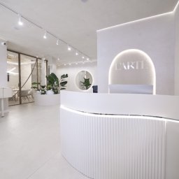 Tofi design - Jasne, minimalistyczne wnętrze biura z recepcją, krzesłem reżyserskim i roślinami doniczkowymi, oświetlone lampami punktowymi i listwami LED.