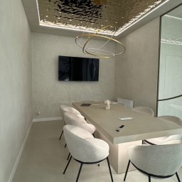 Tofi design - Nowoczesna sala konferencyjna z długim stołem, krzesłami z szarej tkaniny na czarnych nogach, telewizorem na ścianie i dekoracyjnym, lustrzanym sufitem z oświetleniem LED.