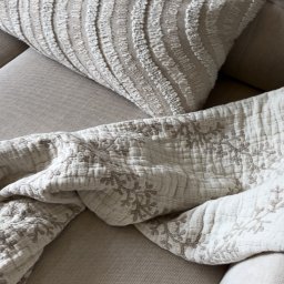 Tofi design - Tekstylia na sofie w odcieniach beżu: dekoracyjna poduszka z tłoczonym wzorem i pikowana narzuta z motywem kwiatowym, Toruń.