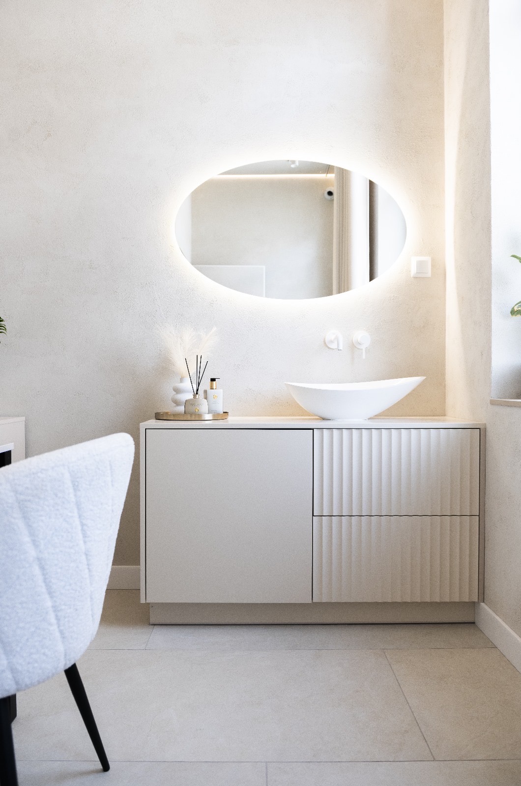 Nowoczesna łazienka w jasnych, stonowanych barwach z owalnym lustrem podświetlanym LED, umywalką nablatową w kształcie łodzi i szafką z frezowanymi frontami.