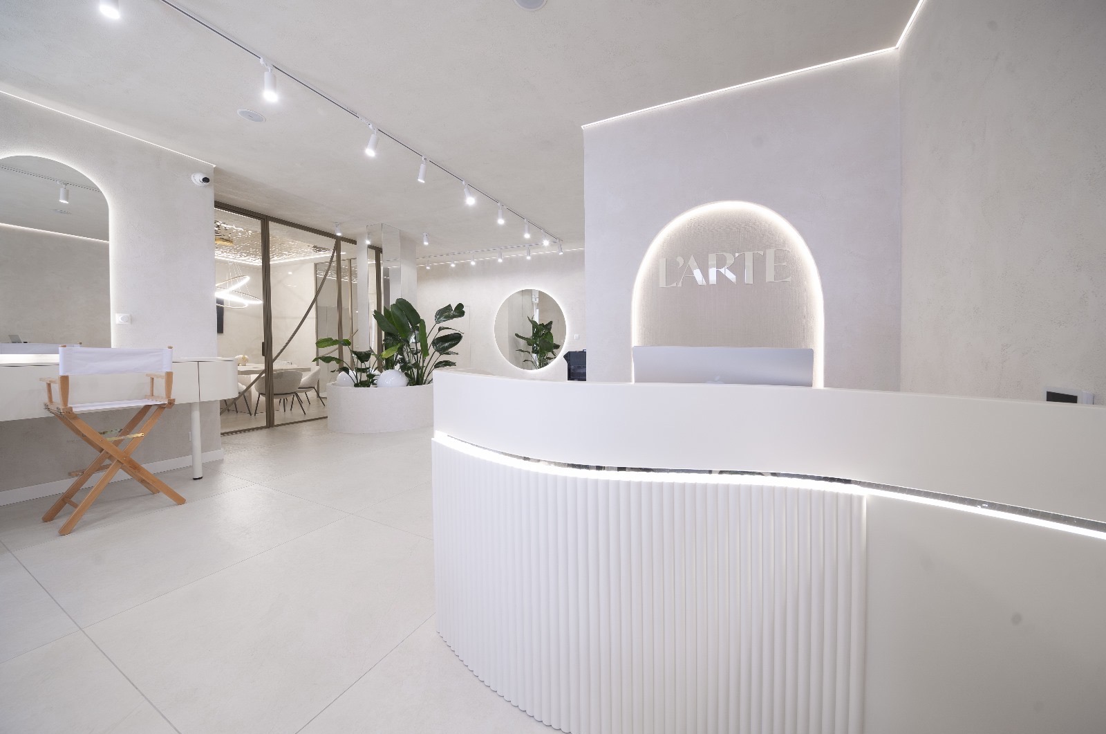 Jasne, minimalistyczne wnętrze biura z recepcją, krzesłem reżyserskim i roślinami doniczkowymi, oświetlone lampami punktowymi i listwami LED.