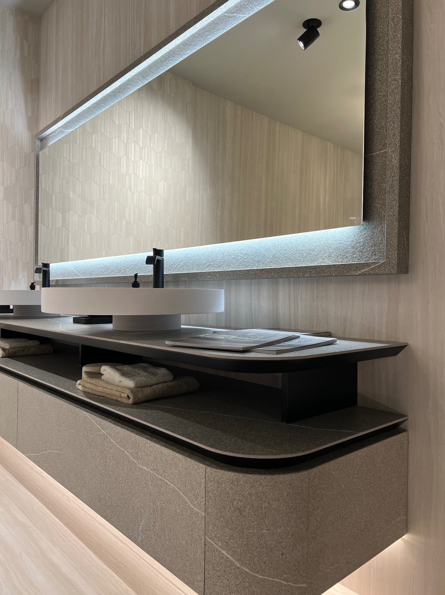Nowoczesna łazienka z dwoma okrągłymi umywalkami nablatowymi, dużym podświetlanym lustrem i szarą szafką z oświetleniem LED u dołu.