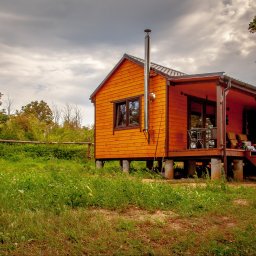 Przedsiębiorstwo Partner Sp. z o.o. - Niewielki, pomarańczowy dom modułowy z kominem, posadowiony na betonowych słupach, otoczony zielenią. Realizacja w Szczecinie.