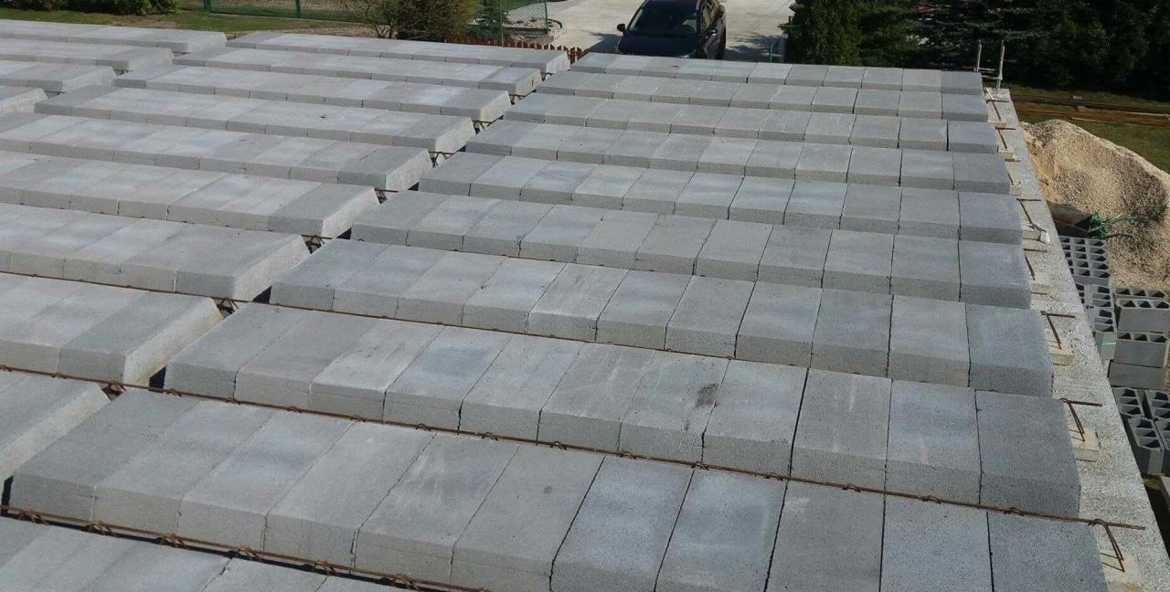 Wznoszenie stropu Teriva z belek i pustaków betonowych, widoczne zbrojenie, w tle zapas pustaków i piasku.