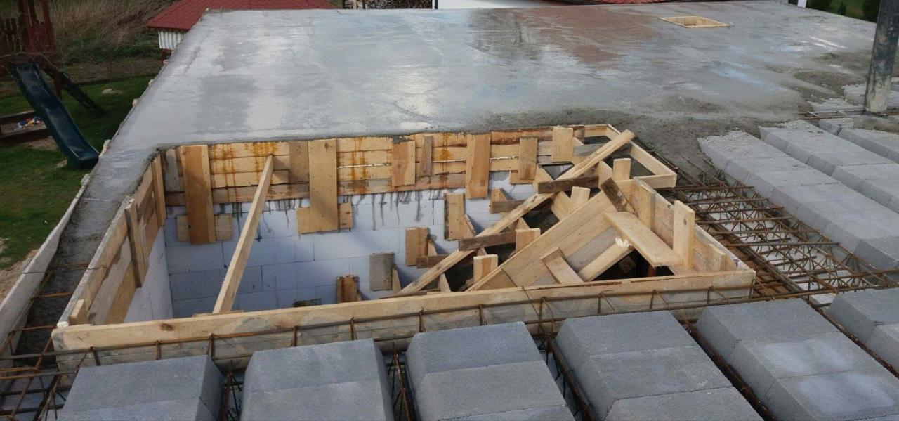 Wylewanie betonowego stropu z deskowaniem otworu, widoczne bloczki betonowe i zbrojenie.