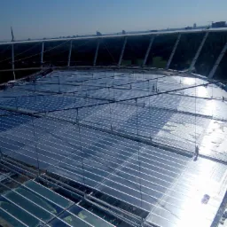 Wysoki kąt widzenia na konstrukcję dachu hali sportowej z widocznymi pracownikami podczas montażu paneli.