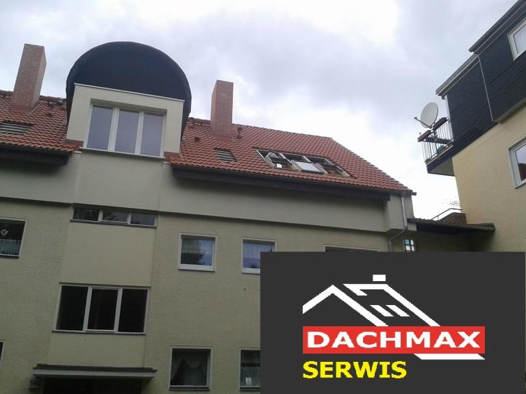 Budynek wielorodzinny z oknami dachowymi, z których jedno jest uszkodzone, widoczne logo firmy Dachmax Serwis.