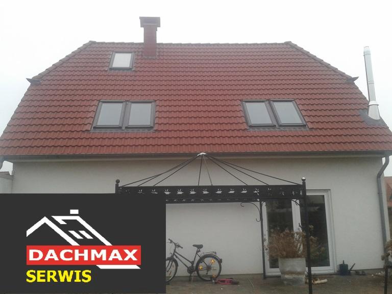 Czerwony dach z trzema oknami dachowymi i kominem, widoczny z poziomu podwórka z rowerem i zadaszeniem, w rogu logo firmy Dachmax Serwis.