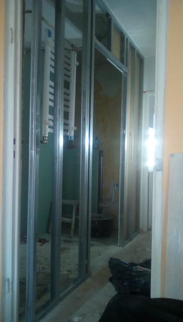 Metalowa konstrukcja szkieletowa ścian działowych w trakcie montażu, widoczny grzejnik na ścianie w tle, pomieszczenie w stanie surowym.