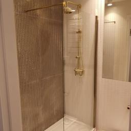 Usługi Budowlane Stanisław Bugajski - Nowoczesna kabina prysznicowa z brodzikiem, złotą armaturą i wzorzystymi płytkami na ścianach, widoczna w trakcie prac wykończeniowych.