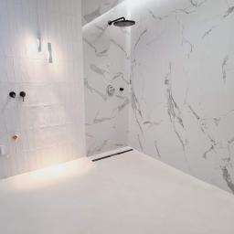 Usługi Budowlane Stanisław Bugajski - Minimalistyczna łazienka z białymi płytkami imitującymi marmur, czarna armatura, podwieszane lampy i odpływ liniowy.