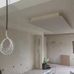 Usługi Budowlane Stanisław Bugajski - Wnętrze w trakcie prac wykończeniowych: częściowo zamontowana płyta gipsowo-kartonowa na suficie, widoczne przewody elektryczne, profile metalowe na podłodze i niedokończone ściany.