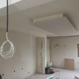 Wnętrze w trakcie prac wykończeniowych: częściowo zamontowana płyta gipsowo-kartonowa na suficie, widoczne przewody elektryczne, profile metalowe na podłodze i niedokończone ściany.