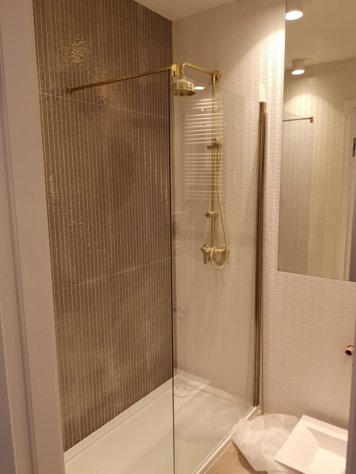 Nowoczesna kabina prysznicowa z brodzikiem, złotą armaturą i wzorzystymi płytkami na ścianach, widoczna w trakcie prac wykończeniowych.