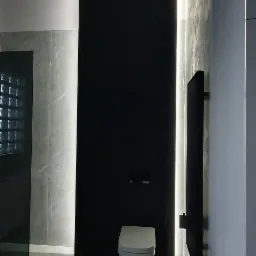 Nowoczesna łazienka z podświetleniem LED, czarną ścianą i wiszącą toaletą, widoczna podłoga z szarych płytek imitujących marmur i fragment kabiny prysznicowej z luksferami.