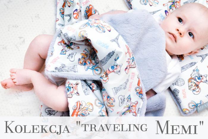 Niemowlę leżące na kocyku i poduszce z motywem podróży po znanych miastach świata: Paryż, Rzym, Londyn, Nowy Jork.
