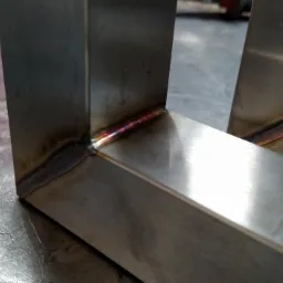 Fragment konstrukcji ze stali nierdzewnej, spawana z profili kwadratowych, widoczne ślady spawania na łączeniach, obróbka metalu w warsztacie.