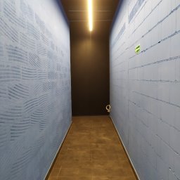 RESIN MADE ART - Korytarz z brązową podłogą z płytek i ścianami pokrytymi niebieską farbą z dekoracyjną fakturą, oświetlony liniową lampą LED na suficie.