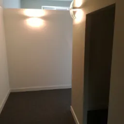 Wnętrze korytarza z szarą podłogą, białymi ścianami i nowoczesnymi lampami ściennymi