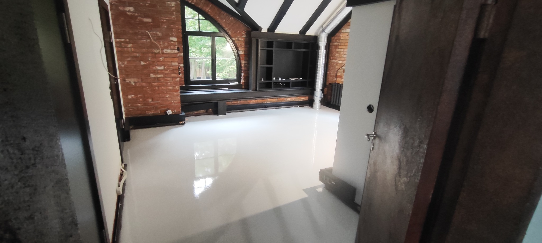 Biała, błyszcząca podłoga w loftowym wnętrzu z ceglaną ścianą, łukowym oknem i czarnymi elementami wykończeniowymi.