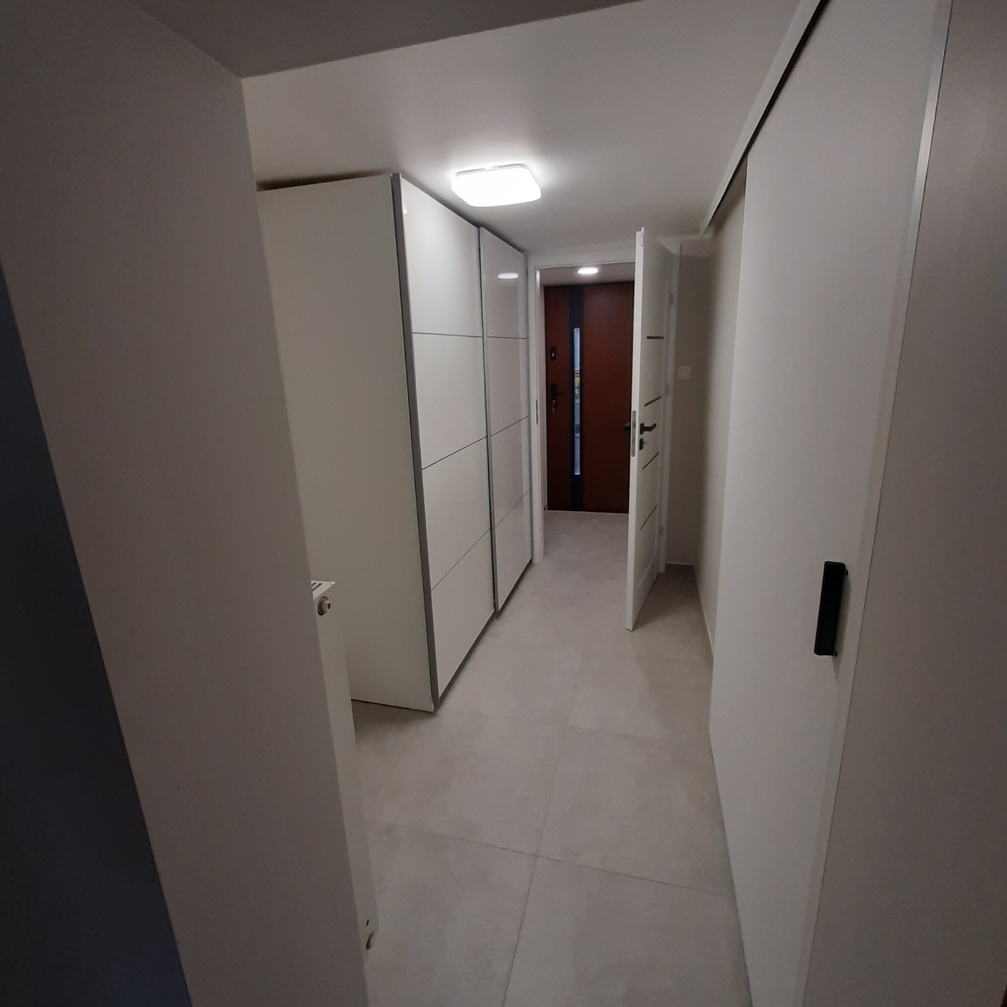 Nowoczesny przedpokój z białymi szafami przesuwnymi i otwartymi drzwiami wejściowymi, widok z perspektywy wnętrza.