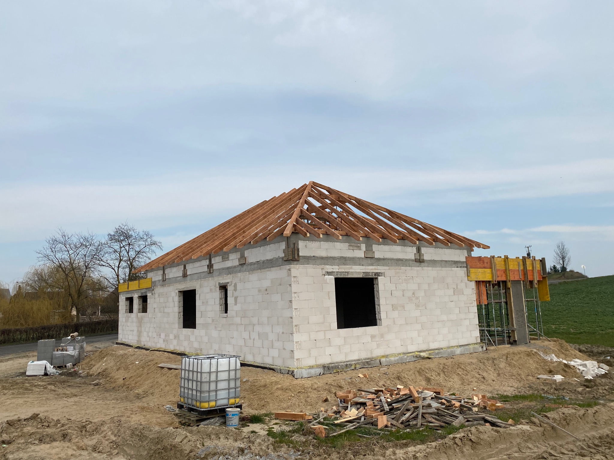 Budowa domu jednorodzinnego w stanie surowym otwartym: ściany z betonu komórkowego, drewniana więźba dachowa, widoczne deskowanie okien i drzwi.