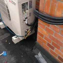 Jednostka zewnętrzna klimatyzacji Mitsubishi Electric zamontowana na dachu, z widocznymi przewodami instalacyjnymi i narzędziami w tle.