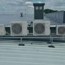 Sandblasting Mateusz Serwinek - Cztery jednostki zewnętrzne klimatyzacji, różnych producentów, zamontowane na metalowej konstrukcji na płaskim dachu budynku przemysłowego, widok z góry.