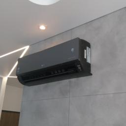 Sandblasting Mateusz Serwinek - Czarna jednostka wewnętrzna klimatyzatora LG zamontowana na szarej ścianie z płytek, podświetlona dekoracyjnym oświetleniem LED na suficie.