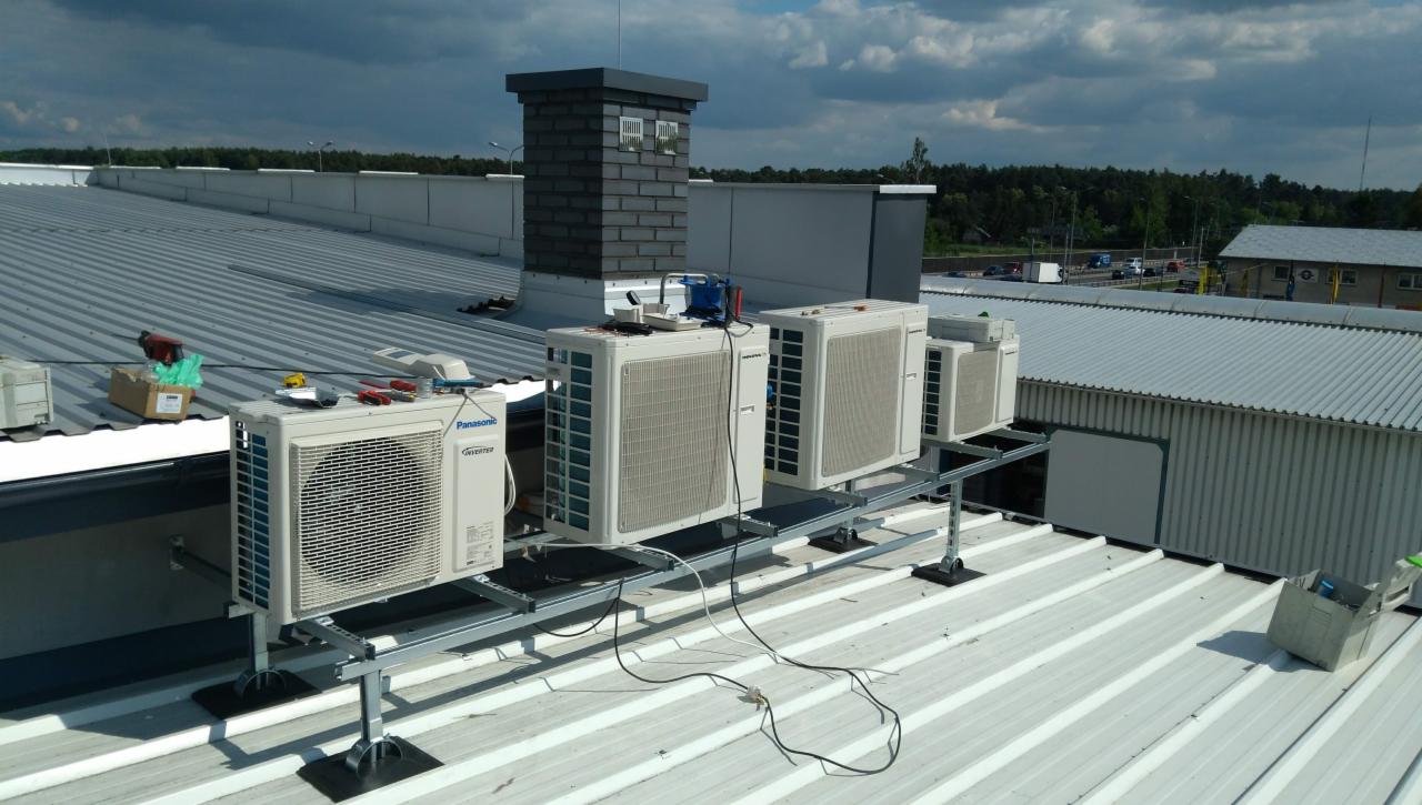 Instalacja rzędu jednostek zewnętrznych na dachu przemysłowym, widoczne narzędzia i materiały montażowe obok pierwszego urządzenia.