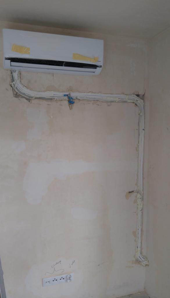 Montaż jednostki wewnętrznej z widocznymi przewodami chłodniczymi i elektrycznymi, zabezpieczonymi pianką montażową na ścianie w trakcie prac wykończeniowych.