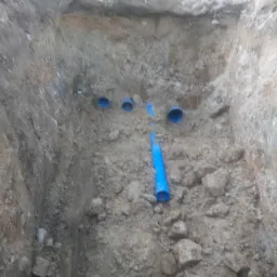 Głęboki wykop w ziemi z widocznymi niebieskimi rurami instalacyjnymi, częściowo połączonymi, z perspektywy z góry.