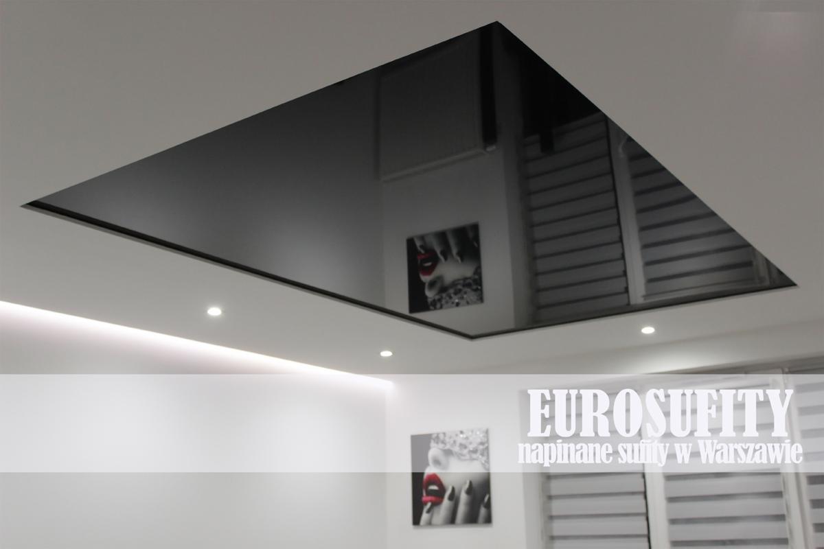 Czarny, lustrzany sufit napinany w kształcie prostokąta, odbijający wnętrze pomieszczenia z obrazami na ścianie i żaluzjami w oknie.