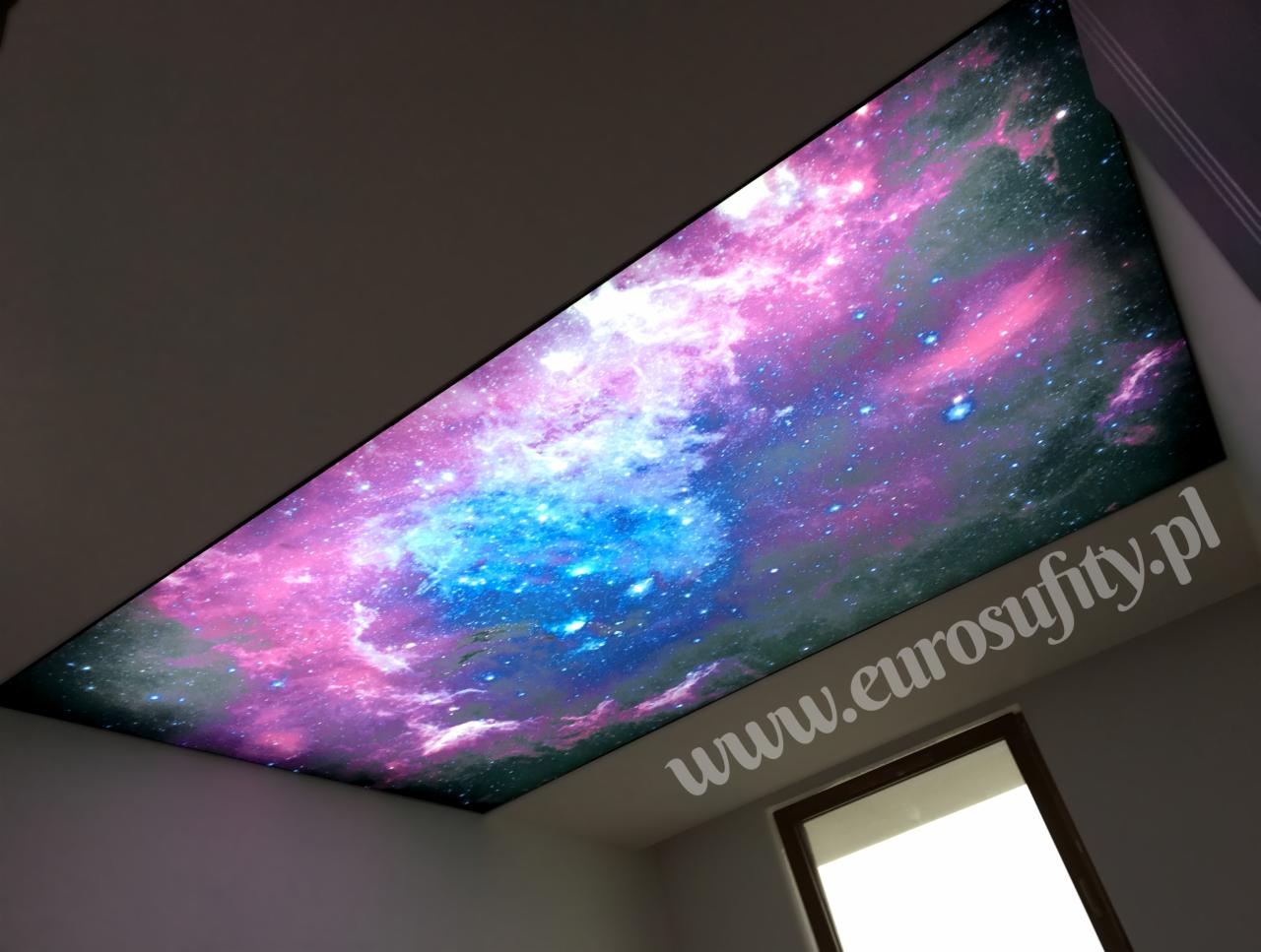 Sufit napinany z motywem kosmosu, widoczny fragment okna i adres strony internetowej na suficie.