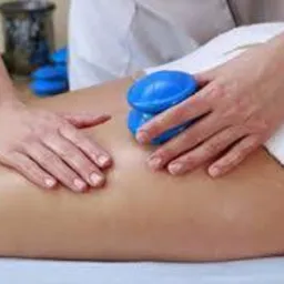 Masaż bańką chińską na plecach pacjenta, widoczne dłonie masażysty i niebieska bańka.