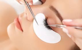 Aplikacja sztucznych rzęs: precyzyjne pincety i biały płatek pod okiem podczas zabiegu przedłużania rzęs.