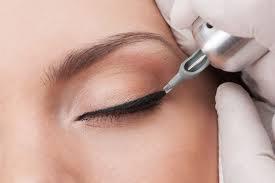 Makijaż permanentny oka: precyzyjna aplikacja czarnego eyelinera wzdłuż linii rzęs, wykonywana przez osobę w białych rękawiczkach. Widoczna igła urządzenia do pigmentacji.