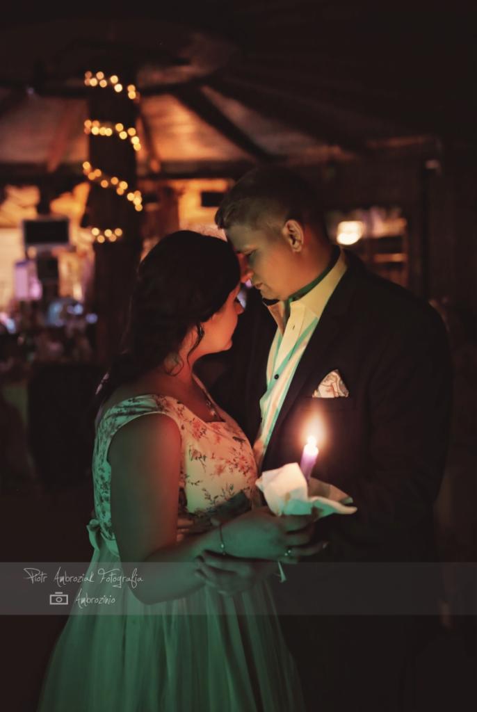Para narzeczonych trzyma zapaloną świecę podczas sesji w rustykalnym wnętrzu z dekoracyjnymi lampkami.