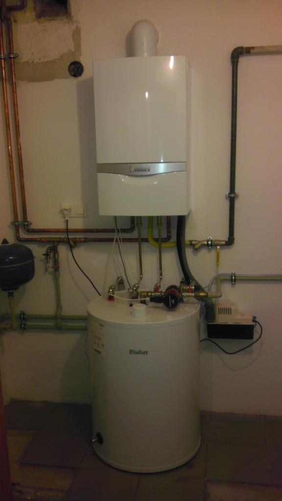 Biały, wiszący piec gazowy z podgrzewaczem wody, marki Vaillant, z widocznymi rurami miedzianymi i instalacją hydrauliczną, zamontowany na ścianie w pomieszczeniu technicznym.