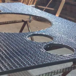 Metalowa krata pomostowa z okrągłymi otworami, spawana konstrukcja na metalowych kozłach w hali produkcyjnej.