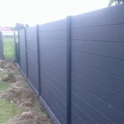 Nowoczesne, grafitowe ogrodzenie panelowe z kompozytu, widoczne świeże ślady prac ziemnych i fragment trawnika.